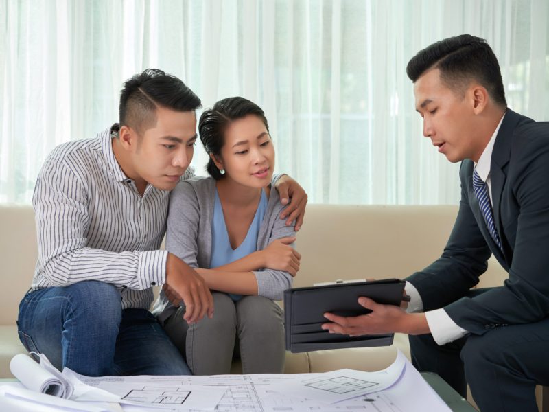 Real estate broker showing photos of house on digital tablet to young couple