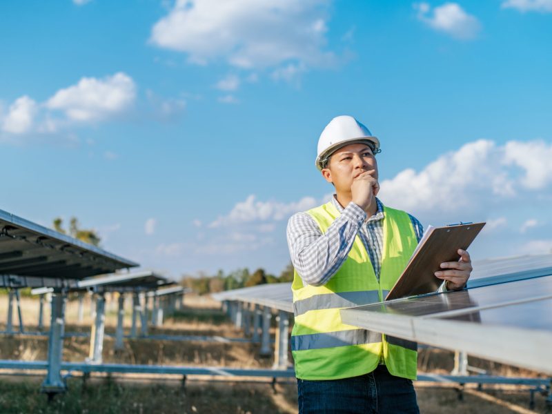 Young Asian Inspector Engineer man working at solar farm, Technician or supervisor male in white helmet Checking operation of sun and photovoltaic solar panel in station, copy space